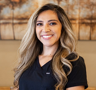 A female dental assistant with blonde hair  wearing black scrubs, background is a painting of trees