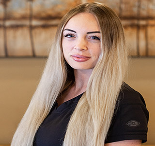 A female dental assistant with blonde hair  wearing black scrubs, background is a painting of trees